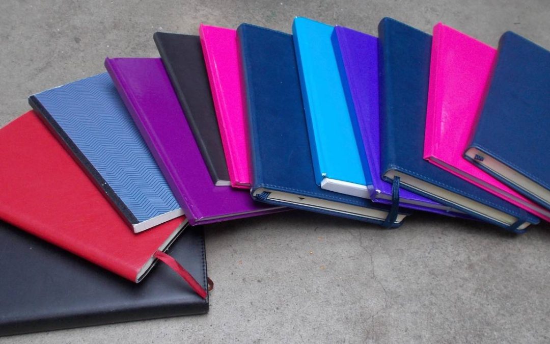 Books with plain coloured covers no text in overlapping horizontal row, covers include red, dark blue, purple, bright pink, light blue, black.